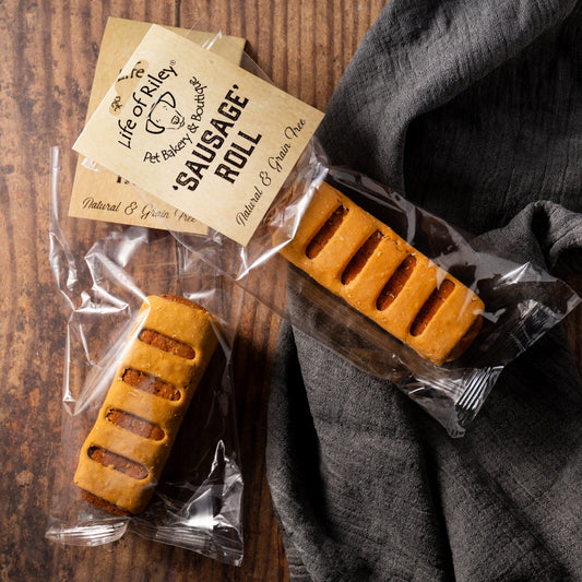 Two sausage rolls in clear packaging with a label on a wooden surface.