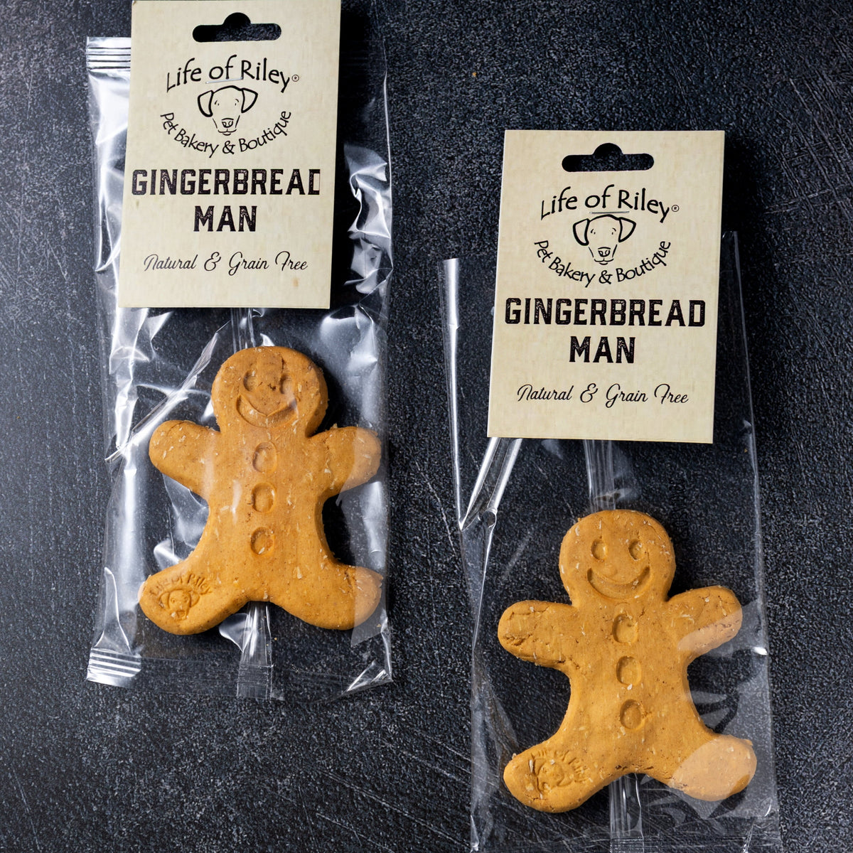Two gingerbread man cookies in clear packaging with labels on a dark surface