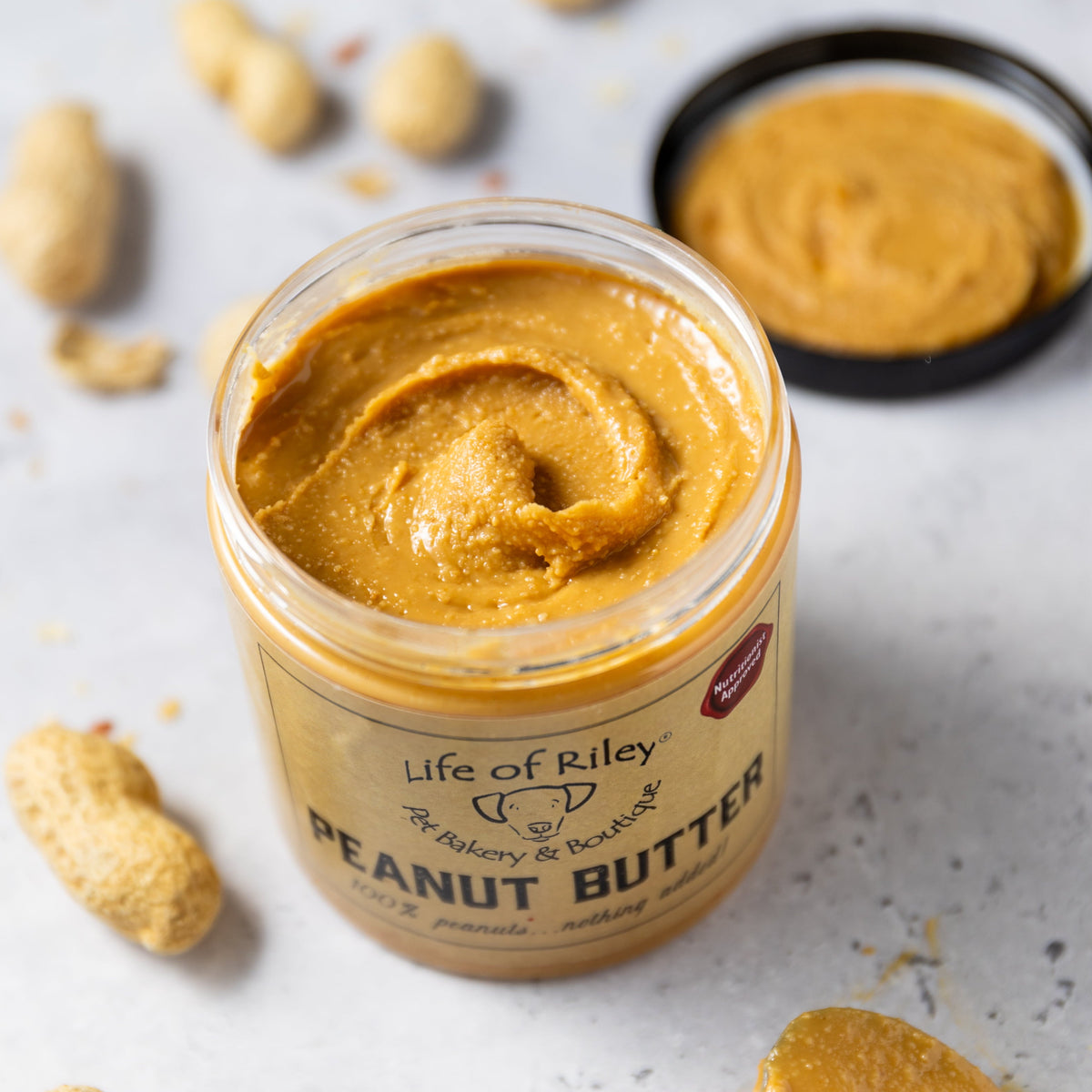 Jar of Life of Riley peanut butter with peanuts around on a light background