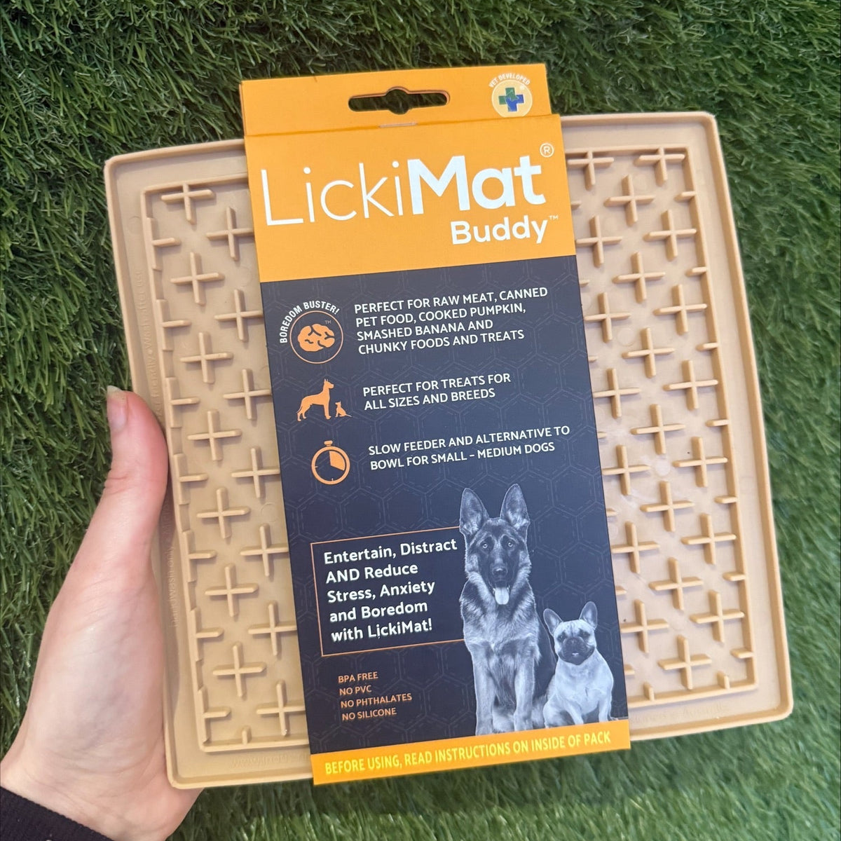 A hand holding a LickiMat Buddy Classic in a beige color, with product information and images of dogs and cats on the packaging.