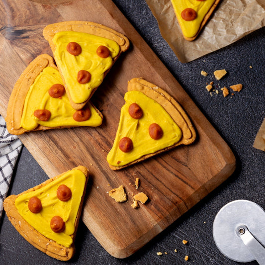 Pizza-themed cookies on a wooden board with a cookie cutter in the background.